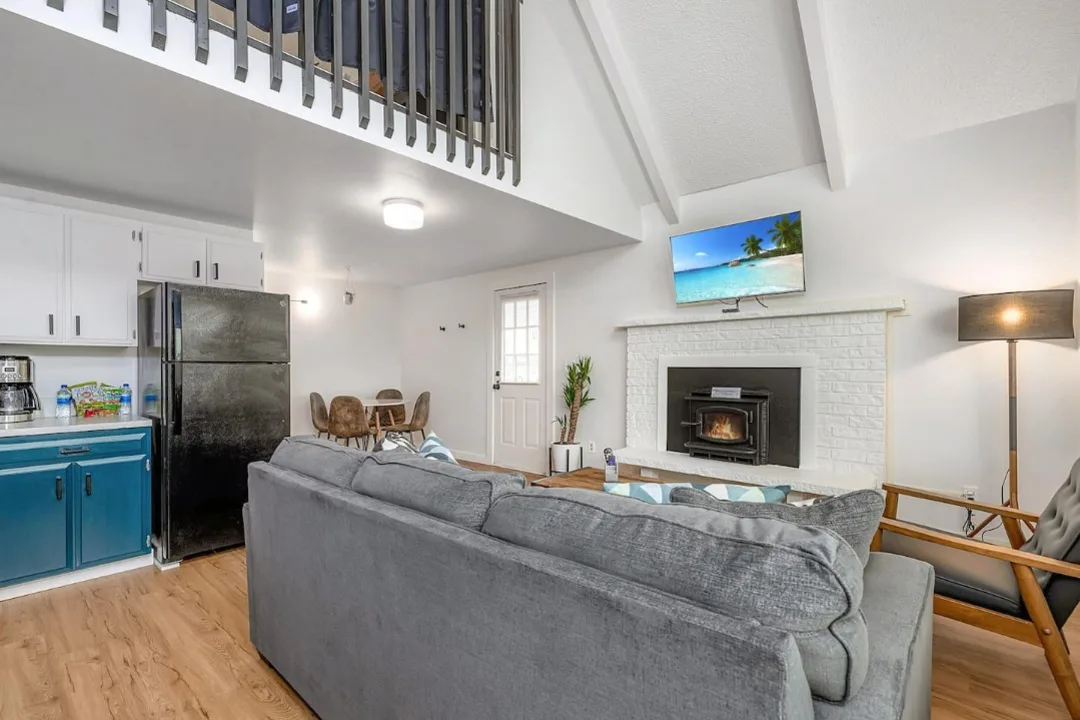 Living room of Tidal House Chalet 1 with a gray sofa, blue kitchen cabinets, and a white fireplace.
