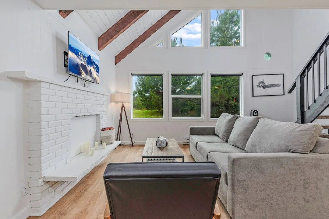 Bright living room of Tidal House Chalet 3 with an exposed wood ceiling beam, gray sofa, and white fireplace.