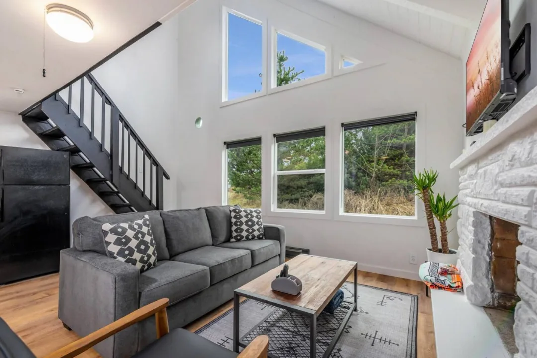 Living room of Tidal House Chalet 4 with a gray sofa, black staircase, and white brick fireplace.