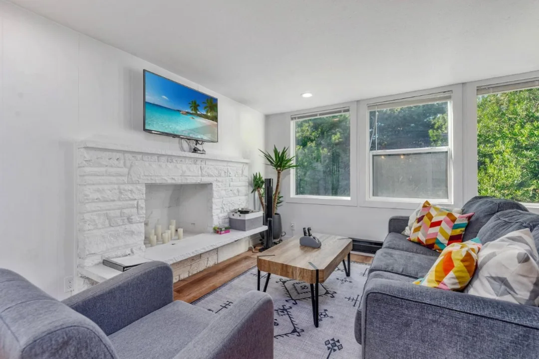 Living room of Tidal House Chalet 5 with gray seating, colorful pillows, and a white stone fireplace.