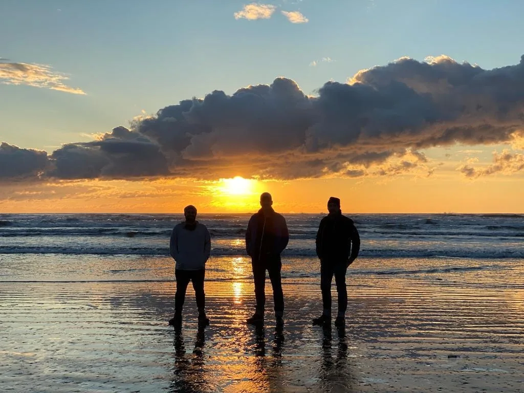 Tidal House's three owners standing on the beach at sunset